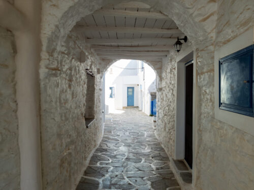 Cyclades destination Greece Kythnos island Chora village. Whitewashed old buildings Greek architecture, stoa arch wooden shelter covers empty narrow cobblestone alley. Summer resort vacation sunny day